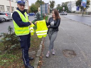 Policjant ruchu drogowego przekazuje kamizelkę odblaskową pieszej