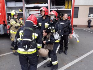 Strażacy wynoszą z budynku ranną kobietę